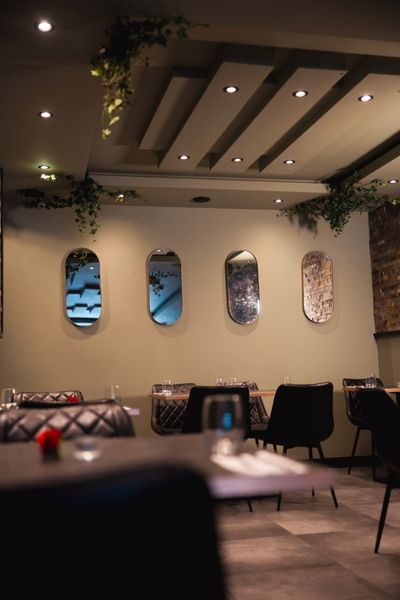 Warmly lit dining room with set tables, hanging greenery and decorative wall panels at Mangia Pizza